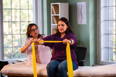 Fizyoterapist Hintli kadın hasta triseps ve omuz güçlendirme egzersizleri yapıyor modern klinikte direnç bandını kullanarak rehabilitasyon ve iyileşme için kıdemli rehberlik altında