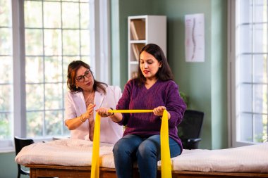 Fizyoterapist Hintli kadın hasta triseps ve omuz güçlendirme egzersizleri yapıyor modern klinikte direnç bandını kullanarak rehabilitasyon ve iyileşme için kıdemli rehberlik altında