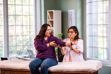 Hintli kadın fizyoterapist, modern klinikte detaylı klinik değerlendirmeler sırasında genç bir kadının dirsek ağrısını inceliyor, ortak bakım ve rehabilitasyon terapisinde uzman olduğunu vurguluyor.