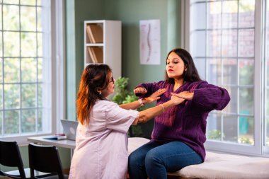 Hintli bayan fizyoterapist, modern klinikte rehberli egzersiz sırasında genç bayan hastalara omuz güçlendirmeyi öğreterek, ağrı kesici ve rehabilitasyon terapisinde uzman olduğunu gösteriyor.