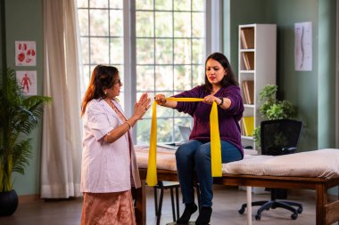 Fizyoterapist Hintli kadın hasta triseps ve omuz güçlendirme egzersizleri yapıyor modern klinikte direnç bandını kullanarak rehabilitasyon ve iyileşme için kıdemli rehberlik altında