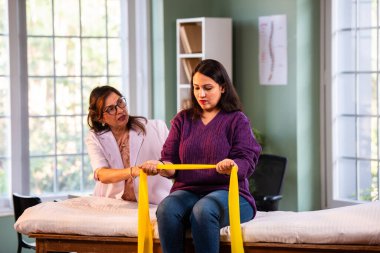 Fizyoterapist Hintli kadın hasta triseps ve omuz güçlendirme egzersizleri yapıyor modern klinikte direnç bandını kullanarak rehabilitasyon ve iyileşme için kıdemli rehberlik altında