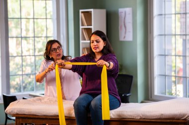Fizyoterapist Hintli kadın hasta triseps ve omuz güçlendirme egzersizleri yapıyor modern klinikte direnç bandını kullanarak rehabilitasyon ve iyileşme için kıdemli rehberlik altında