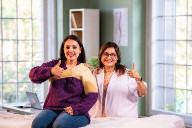 Hintli bayan fizyoterapist genç bayan hastaların omuz ağrılarını tedavi ederken modern klinikte omuz desteği desteği takıyor ve yaralanma yönetimi ve rehabilitasyon konusunda uzman olduğunu gösteriyor.