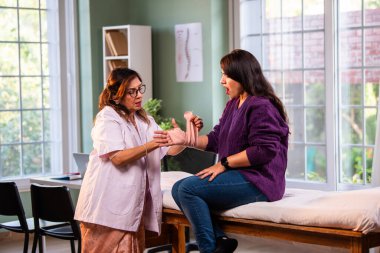 Hintli kadın fizyoterapist, modern klinikte tedavi sırasında genç bayan hastalara bilek desteği uygular, hastanın baş parmağı gösterirken, ağrıyı ve yaralanmayı uzmanlıkla ele alır.