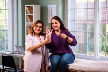 Hintli kadın fizyoterapist, modern klinikte tedavi sırasında genç bayan hastalara bilek desteği uygular, hastanın baş parmağı gösterirken, ağrıyı ve yaralanmayı uzmanlıkla ele alır.