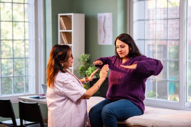 Hintli bayan fizyoterapist, modern klinikte rehberli egzersiz sırasında genç bayan hastalara omuz güçlendirmeyi öğreterek, ağrı kesici ve rehabilitasyon terapisinde uzman olduğunu gösteriyor.