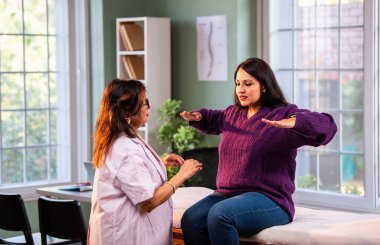 Hintli bayan fizyoterapist, modern klinikte rehberli egzersiz sırasında genç bayan hastalara omuz güçlendirmeyi öğreterek, ağrı kesici ve rehabilitasyon terapisinde uzman olduğunu gösteriyor.