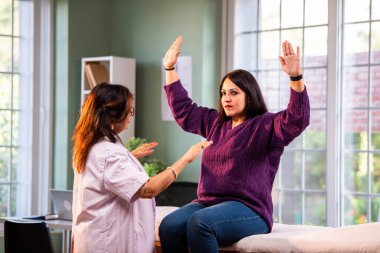 Hintli bayan fizyoterapist, modern klinikte rehberli egzersiz sırasında genç bayan hastalara omuz güçlendirmeyi öğreterek, ağrı kesici ve rehabilitasyon terapisinde uzman olduğunu gösteriyor.