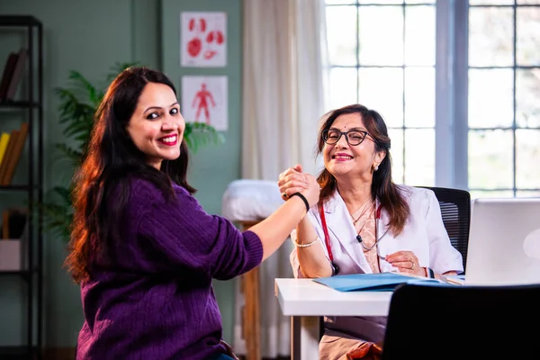 Modern klinikte gülümseyen, kıdemli tıbbi uzmanlık, hasta güveni, pozitif sağlık ilişkisi ve kendine güven gösteren Hintli kadın doktor kameraya bakıyor.