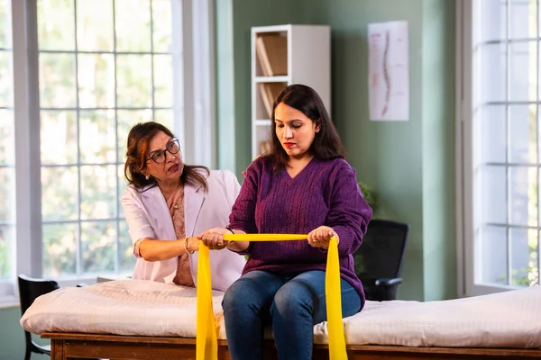 Fizyoterapist Hintli kadın hasta triseps ve omuz güçlendirme egzersizleri yapıyor modern klinikte direnç bandını kullanarak rehabilitasyon ve iyileşme için kıdemli rehberlik altında