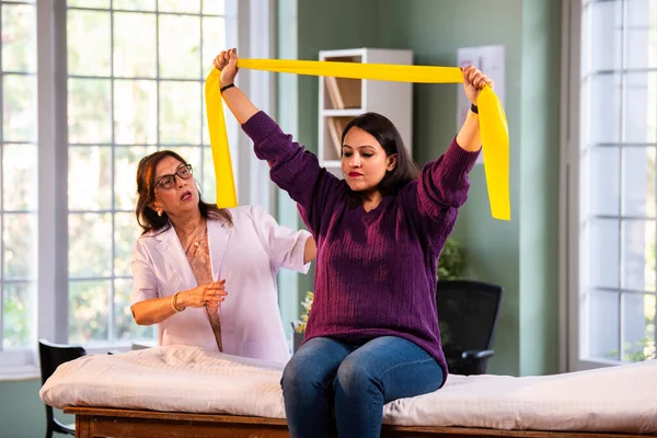 Fizyoterapist Hintli kadın hasta triseps ve omuz güçlendirme egzersizleri yapıyor modern klinikte direnç bandını kullanarak rehabilitasyon ve iyileşme için kıdemli rehberlik altında