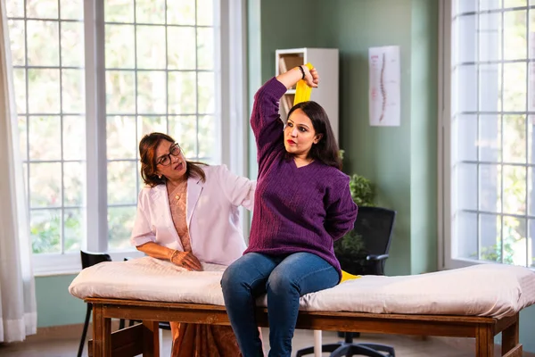 Fizyoterapist Hintli kadın hasta triseps ve omuz güçlendirme egzersizleri yapıyor modern klinikte direnç bandını kullanarak rehabilitasyon ve iyileşme için kıdemli rehberlik altında