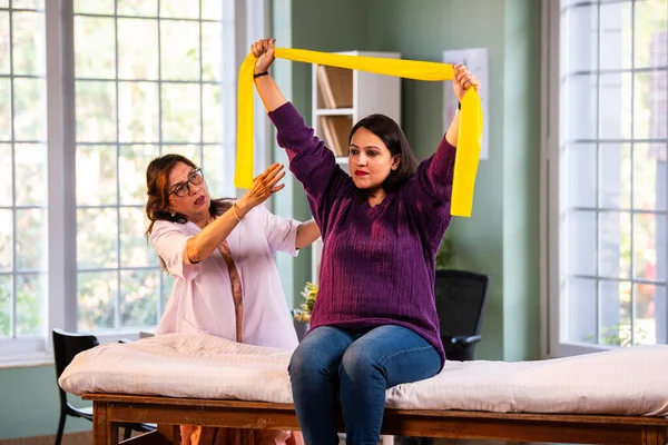 Fizyoterapist Hintli kadın hasta triseps ve omuz güçlendirme egzersizleri yapıyor modern klinikte direnç bandını kullanarak rehabilitasyon ve iyileşme için kıdemli rehberlik altında