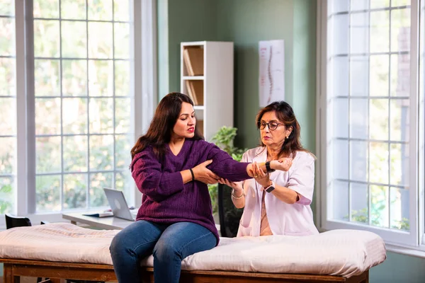 Hintli kadın fizyoterapist, modern klinikte detaylı klinik değerlendirmeler sırasında genç bir kadının dirsek ağrısını inceliyor, ortak bakım ve rehabilitasyon terapisinde uzman olduğunu vurguluyor.