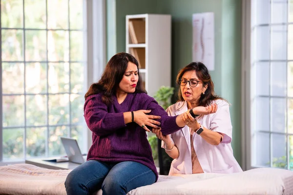 Hintli kadın fizyoterapist, modern klinikte detaylı klinik değerlendirmeler sırasında genç bir kadının dirsek ağrısını inceliyor, ortak bakım ve rehabilitasyon terapisinde uzman olduğunu vurguluyor.