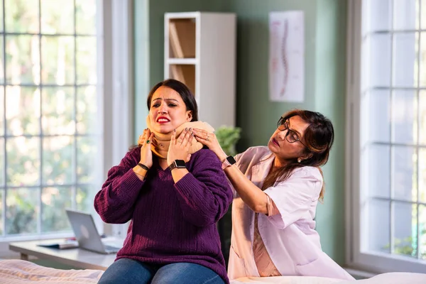 Hintli kadın fizyoterapist, modern klinikte boyun ağrısını tedavi ederken boyun tasmasını takıyor. İkisi de iyileşme sürecinde iyi niyet ve güven gösteriyor.