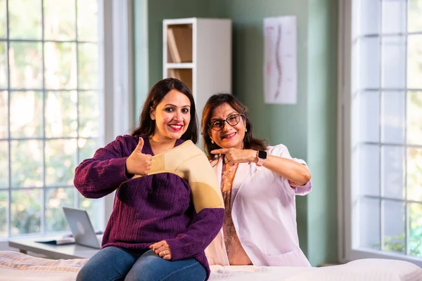 Hintli bayan fizyoterapist genç bayan hastaların omuz ağrılarını tedavi ederken modern klinikte omuz desteği desteği takıyor ve yaralanma yönetimi ve rehabilitasyon konusunda uzman olduğunu gösteriyor.