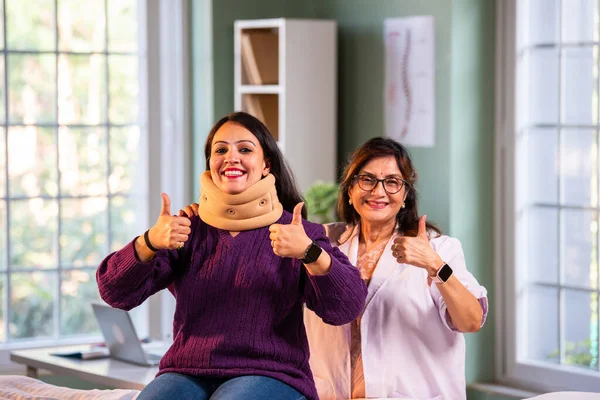 Hintli kadın fizyoterapist, modern klinikte boyun ağrısını tedavi ederken boyun tasmasını takıyor. İkisi de iyileşme sürecinde iyi niyet ve güven gösteriyor.