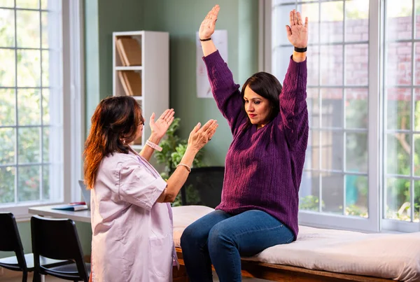 Hintli bayan fizyoterapist, modern klinikte rehberli egzersiz sırasında genç bayan hastalara omuz güçlendirmeyi öğreterek, ağrı kesici ve rehabilitasyon terapisinde uzman olduğunu gösteriyor.