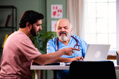 Hintli erkek doktor, deneyimli bir doktor olarak genç bir hastaya danışmanlık yaparken dizüstü bilgisayar kullanarak modern Hint kliniğinde OPD sağlık danışmanlığı hakkında konuşuyor.