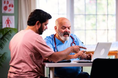 Hintli erkek doktor, deneyimli bir doktor olarak genç bir hastaya danışmanlık yaparken dizüstü bilgisayar kullanarak modern Hint kliniğinde OPD sağlık danışmanlığı hakkında konuşuyor.