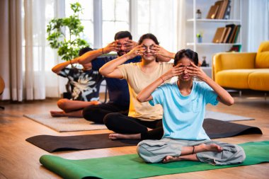 Dört kişilik Hint ailesi: bhramari pranayama ya da arı nefes egzersizi. Yoga stilinde sağlık sağlığını destekleyen modern bir evde sakin bir sabah saatlerinde evde birlikte yojik nefes alma egzersizi yapıyorlar.