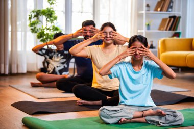 Dört kişilik Hint ailesi: bhramari pranayama ya da arı nefes egzersizi. Yoga stilinde sağlık sağlığını destekleyen modern bir evde sakin bir sabah saatlerinde evde birlikte yojik nefes alma egzersizi yapıyorlar.