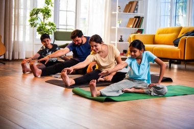Hintli aile evde yog asana yapıyor Janu shirasana pratik yapıyor sakin bir sabah saatlerinde evde birlikte diz boyu yoga yapıyorlar modern savurgan bir yaşam alanında sağlıklı bir yaşam tarzını destekliyorlar.