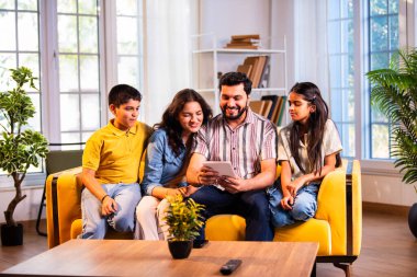Hintli genç bir aile, evde eski fotoğrafları seyrederken birlikte mutlu anıları hatırlarken modern bir oturma odasındaki kanepede oturup gülüşmeler, duygusal aile anlarının tadını çıkarıyordu.