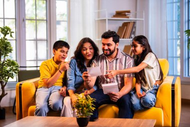 Hintli genç bir aile, evde eski fotoğrafları seyrederken birlikte mutlu anıları hatırlarken modern bir oturma odasındaki kanepede oturup gülüşmeler, duygusal aile anlarının tadını çıkarıyordu.