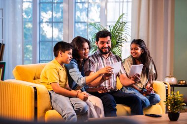 Hintli genç bir aile, evde eski fotoğrafları seyrederken birlikte mutlu anıları hatırlarken modern bir oturma odasındaki kanepede oturup gülüşmeler, duygusal aile anlarının tadını çıkarıyordu.