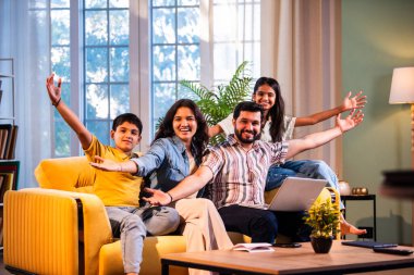 Hintli genç bir aile evlerinde dizüstü bilgisayar kullanıyor. Kanepede birlikte oturuyor. İnternette sörf yapıyor ve içeriden alışveriş yapıyor.