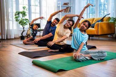 Hint ailesi evde yog asana yapıyor. Parsva Sukhasana antrenmanı yapıyorlar. Yan yana oturup yoga yapıyorlar.