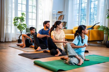 Hint ailesi evde yog asana yapıyor. Matsyendrasana, sakin bir sabah saatinde evde birlikte omurga bükme yogası yapıyor. Modern, savurgan bir yaşam alanında, sağlığını destekliyor.