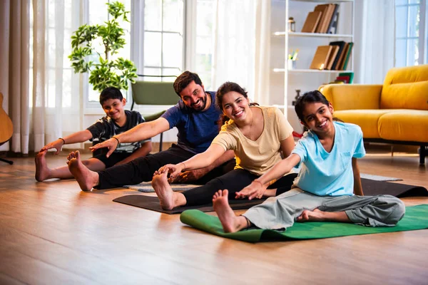 Hintli aile evde yog asana yapıyor Janu shirasana pratik yapıyor sakin bir sabah saatlerinde evde birlikte diz boyu yoga yapıyorlar modern savurgan bir yaşam alanında sağlıklı bir yaşam tarzını destekliyorlar.
