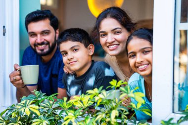 Hintli genç bir aile pencereden dışarı bakıp gülümsüyor ve birbirine işaret ediyor. Bu arada evde genç ebeveynler oğullarıyla ve kızlarıyla birlikte modern, gösterişli bir apartmanın içinde şehir manzarasının tadını çıkarıyorlar.