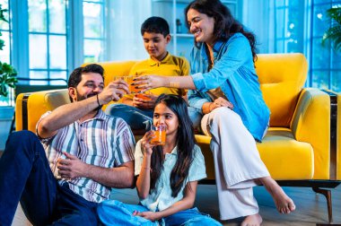 Hintli aile birlikte soğuk bardakta içki içerken, anne kocaya ve çocuklara ferahlatıcı içecekler ikram ederken, modern müsrif evde herkes mutlu vakit geçirmenin keyfini çıkarıyor.