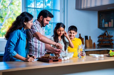 Hint ailesi, modern mutfakta kek hamuru yaparken genç ebeveynler, hamuru karıştırırken kaliteli zaman geçirmenin, bağ kurmanın ve neşeli ev yemeği pişirmenin keyfini çıkarıyorlar.