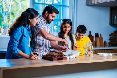 Hint ailesi, modern mutfakta kek hamuru yaparken genç ebeveynler, hamuru karıştırırken kaliteli zaman geçirmenin, bağ kurmanın ve neşeli ev yemeği pişirmenin keyfini çıkarıyorlar.