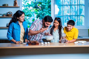 Hint ailesi, modern mutfakta kek hamuru yaparken genç ebeveynler, hamuru karıştırırken kaliteli zaman geçirmenin, bağ kurmanın ve neşeli ev yemeği pişirmenin keyfini çıkarıyorlar.
