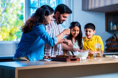 Hint ailesi, modern mutfakta kek hamuru yaparken genç ebeveynler, hamuru karıştırırken kaliteli zaman geçirmenin, bağ kurmanın ve neşeli ev yemeği pişirmenin keyfini çıkarıyorlar.