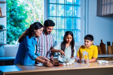 Hint ailesi, modern mutfakta kek hamuru yaparken genç ebeveynler, hamuru karıştırırken kaliteli zaman geçirmenin, bağ kurmanın ve neşeli ev yemeği pişirmenin keyfini çıkarıyorlar.