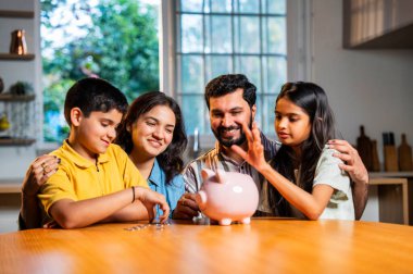 Modern evdeki domuz kumbarasında dört madeni paradan oluşan Hintli genç aile, erkek ve kız çocuklarına para disiplini, finansal planlama, gelecekteki güvenlik ve iyi tasarruf alışkanlıklarının önemini öğretiyor.