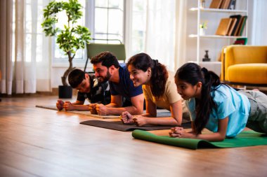 Hint ailesi, modern, müsrif bir yaşam alanında aile fitness seansı sırasında evde oturup, çekirdek kuvveti alıştırması yapıyor ve evde neşeli bir ruh hali sergiliyor.