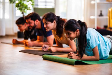 Hint ailesi, modern, müsrif bir yaşam alanında aile fitness seansı sırasında evde oturup, çekirdek kuvveti alıştırması yapıyor ve evde neşeli bir ruh hali sergiliyor.