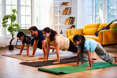 Hintli aile evde Suryanamaskara yapıyor. Sağlıklı vücut için evde güneş selamı yogası yapıyorlar. Ve sabahları modern, savurgan bir yaşam alanında sakin bir zihin.