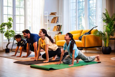 Hintli aile evde Suryanamaskara yapıyor. Sağlıklı vücut için evde güneş selamı yogası yapıyorlar. Ve sabahları modern, savurgan bir yaşam alanında sakin bir zihin.