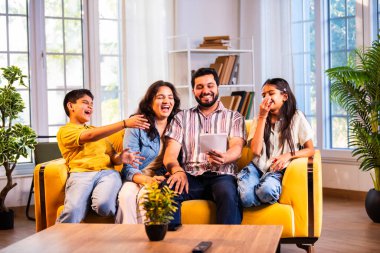 Hintli genç bir aile, evde eski fotoğrafları seyrederken birlikte mutlu anıları hatırlarken modern bir oturma odasındaki kanepede oturup gülüşmeler, duygusal aile anlarının tadını çıkarıyordu.