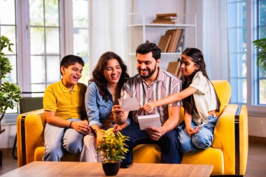 Hintli genç bir aile, evde eski fotoğrafları seyrederken birlikte mutlu anıları hatırlarken modern bir oturma odasındaki kanepede oturup gülüşmeler, duygusal aile anlarının tadını çıkarıyordu.